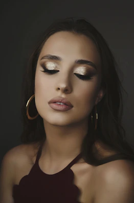 Elegant party makeup look featuring shimmering eyeshadow and a sleek updo against a rose gold backdrop.