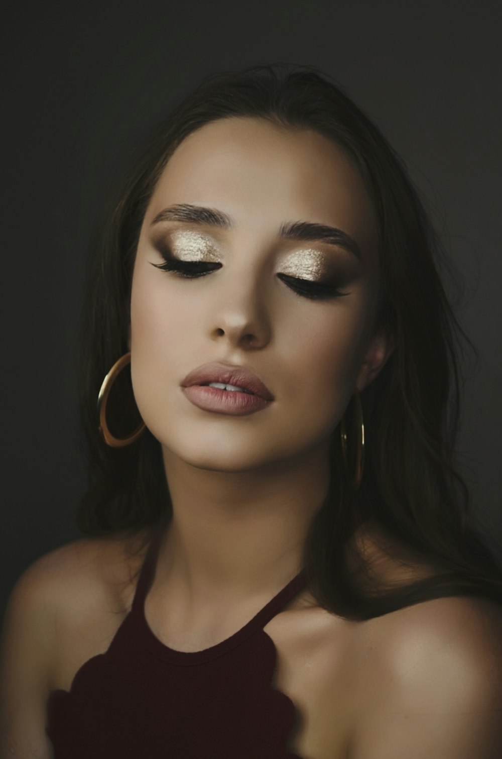 woman in maroon halter top, gold-colored hoop earrings, and gold eyeshadow