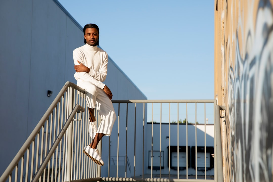 man wearing white long-sleeved shirt sitting on gray stainless steel railings