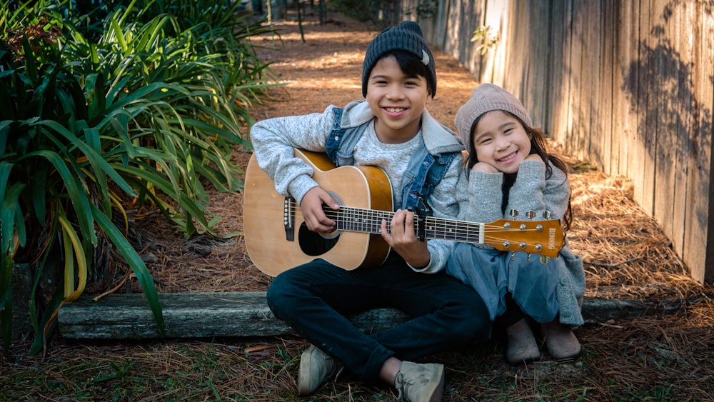 boy holding dreadnought acoustic guitar beside girl during daytime