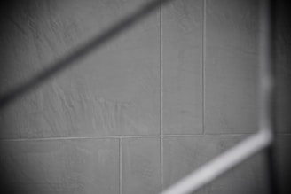 Gray tiles with visible grout lines form a geometric pattern, intersected by a soft, diagonal shadow.