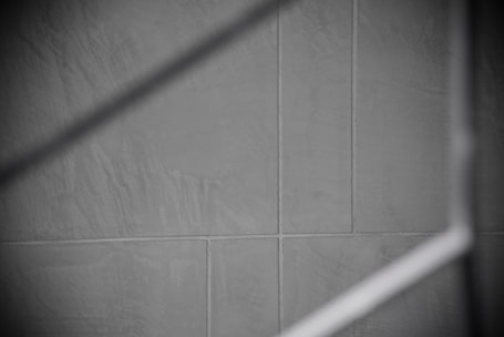 Gray tiles with visible grout lines form a geometric pattern, intersected by a soft, diagonal shadow.