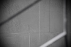 Gray tiles with visible grout lines form a geometric pattern, intersected by a soft, diagonal shadow.