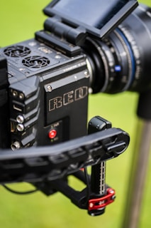 Close-up view of a professional RED camera with visible buttons, HDMI port, lens, and display screen on a green blurred background.