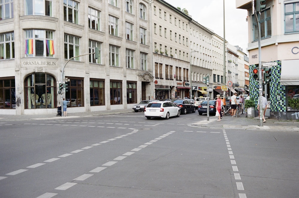 people walking on pathway and vehicles on road beside buildings during daytime