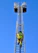 A firefighter is climbing a tall metal ladder on a fire truck, reaching towards two platforms against a clear blue sky. The firefighter is wearing protective gear, including a helmet and high-visibility jacket.