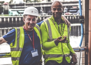 selective focus photography of two men standing side by side wearing green reflective vests