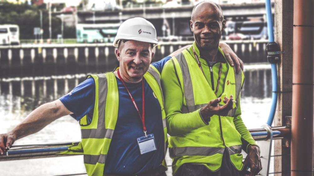 selective focus photography of two men standing side by side wearing green reflective vests