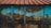 A weathered and rusted metal sheet is supported by vertical wooden beams, featuring a combination of blue paint and brown rust stains. The metal is topped with a corrugated roof of reddish-brown tin.