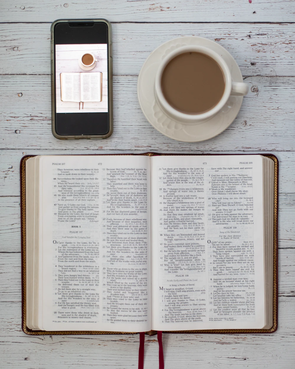 An open Bible beside a cup of coffee and a phone