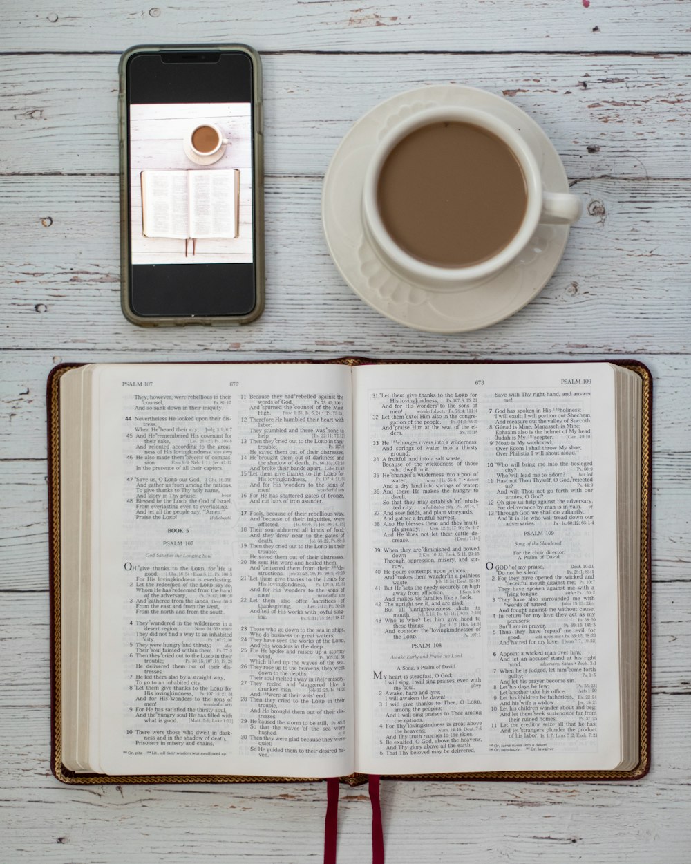 테이블 위에 놓인 커피 한 잔과 스마트폰 옆에 펼쳐진 성경