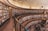 A large, circular library with multiple levels of bookshelves filled with a diverse collection of books. The architecture features wooden elements and a high, curved ceiling. There are a few people reading and interacting on the lower level, some sitting on chairs and others walking around.