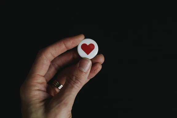 person holding red and white hear button
