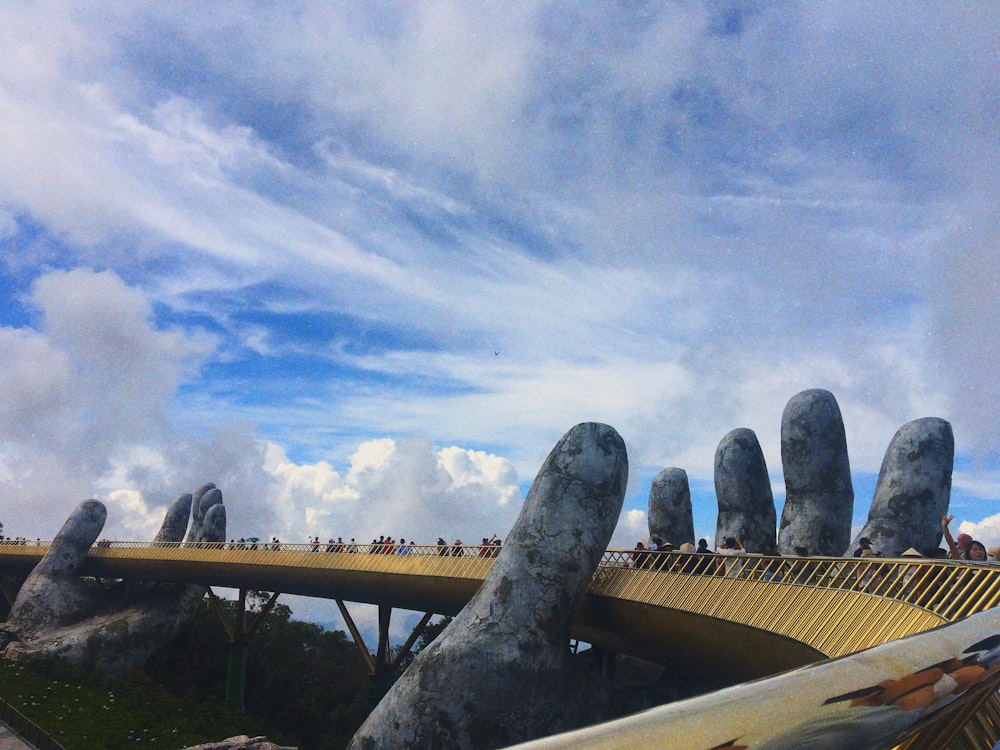 pessoas caminhando na ponte com escultura de mãos humanas durante o dia