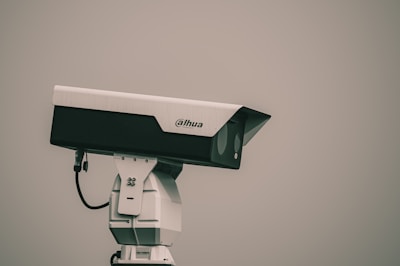 A surveillance camera mounted on a white stand, positioned against a plain background. The camera is branded with the logo 'Dahua' and appears to be pointed to the right.