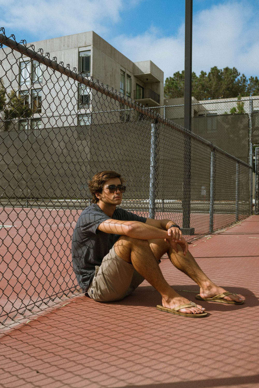 man wearing black crew-neck t-shirt sitting and leaning against chain link fence