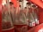Rows of empty, clear glass bottles with red and white labels are neatly arranged in a red plastic crate. The bottles are positioned closely together, showcasing a familiar logo associated with a popular soft drink. The inner surfaces of the crate have slots that hold the bottles securely.