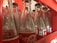 Rows of empty, clear glass bottles with red and white labels are neatly arranged in a red plastic crate. The bottles are positioned closely together, showcasing a familiar logo associated with a popular soft drink. The inner surfaces of the crate have slots that hold the bottles securely.