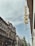 A street view featuring classic European architecture with ornate facades and a tall, narrow sign reading 'Otthon' attached to the side of a building. The sky is overcast with a hint of blue peeking through.