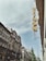 A street view featuring classic European architecture with ornate facades and a tall, narrow sign reading 'Otthon' attached to the side of a building. The sky is overcast with a hint of blue peeking through.