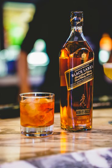 Copo de whisky com gelo sobre balcão de bar