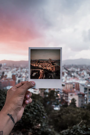 Close-up of a vibrant Polaroid photo held by a hand against a colorful urban street backdrop.