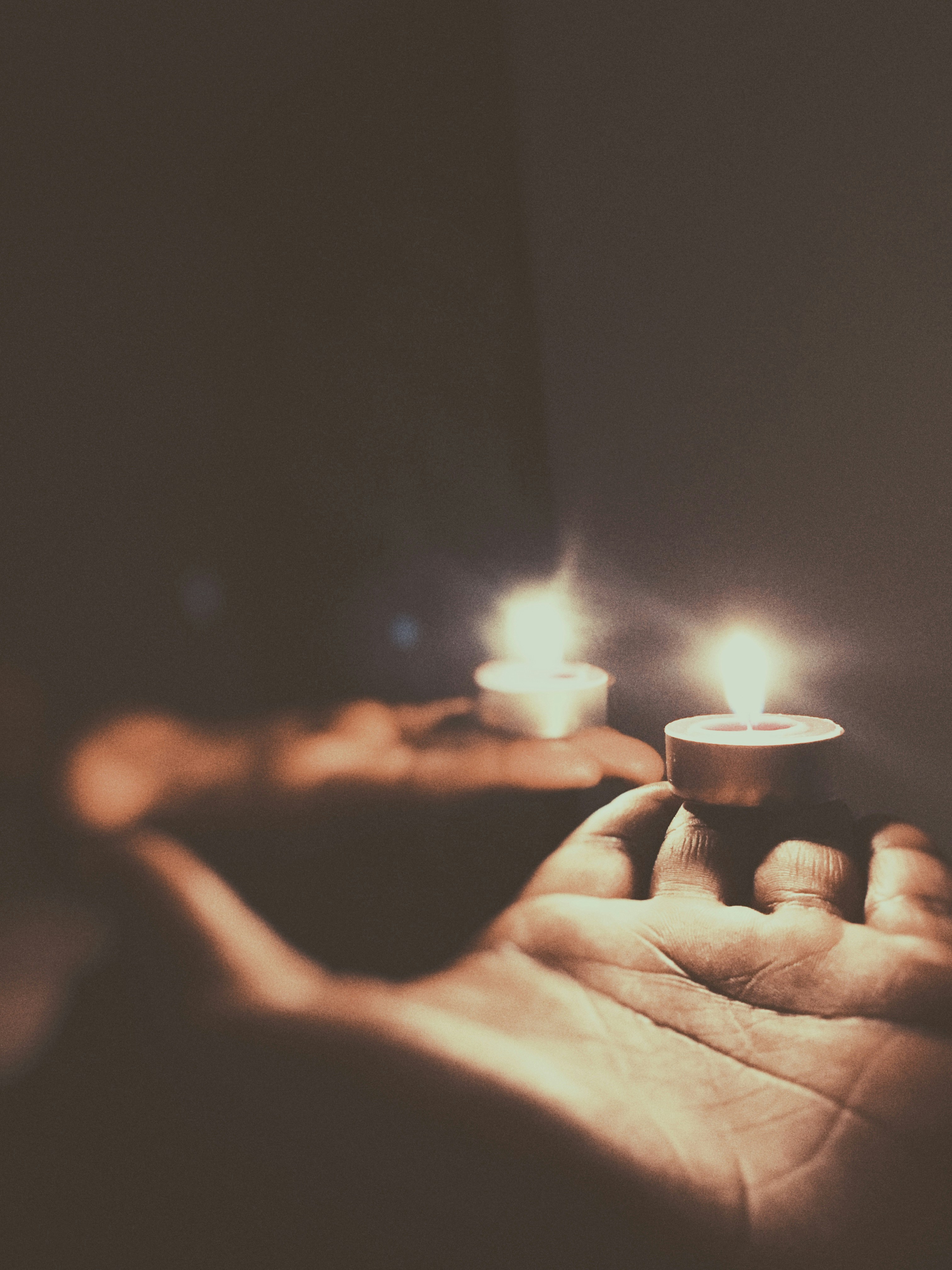 A close-up of hands holding candles glowing softly in a dim room.