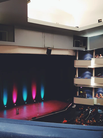 An empty stage bathed in soft white and blue lights, framed by the two classic drama masks.