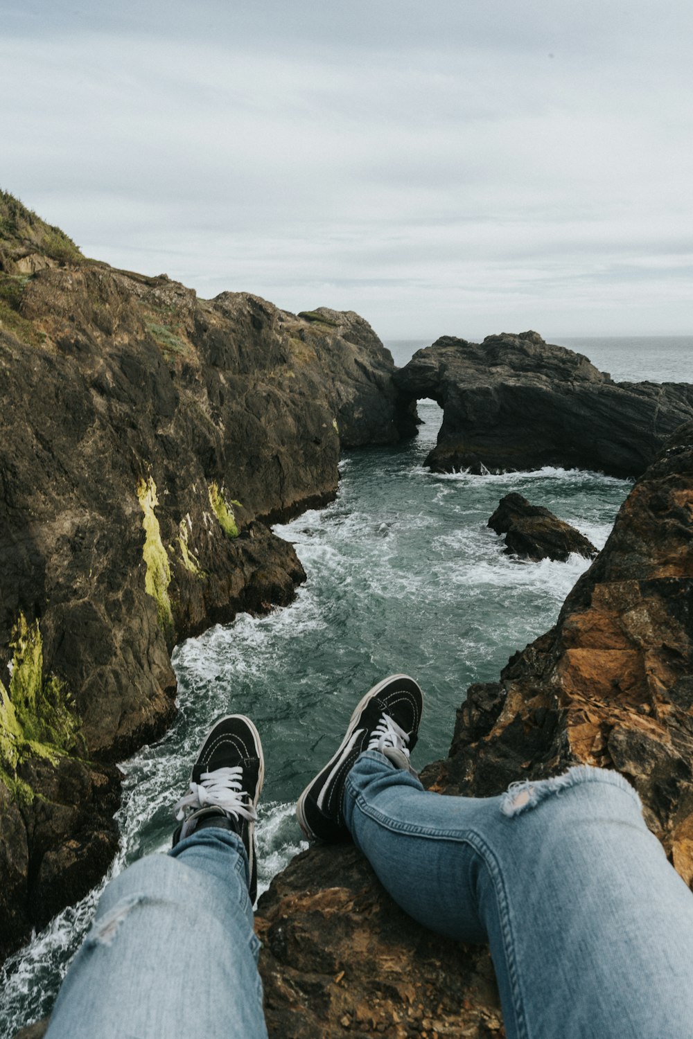 sitting person wearing gray denim distressed jeans on cliff