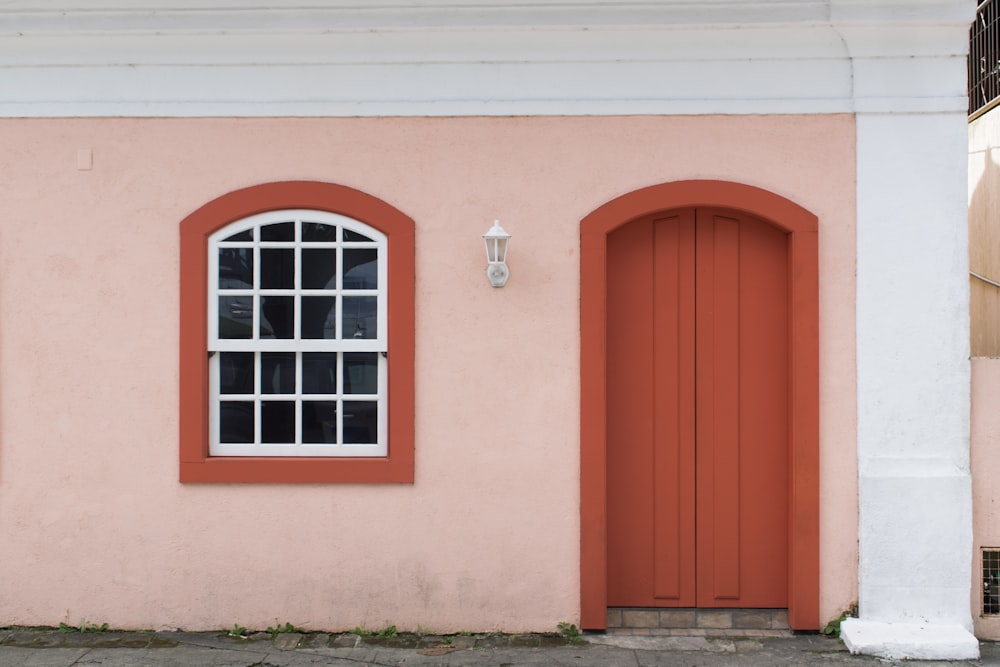 Casa de concreto rosa mostrando porta de madeira laranja fechada