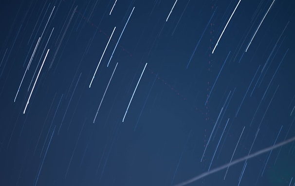 Long exposure photograph capturing star trails across a dark night sky, with smooth streaks of light creating dynamic, linear patterns.