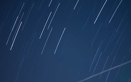 Long exposure photograph capturing star trails across a dark night sky, with smooth streaks of light creating dynamic, linear patterns.