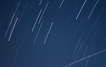 Long exposure photograph capturing star trails across a dark night sky, with smooth streaks of light creating dynamic, linear patterns.