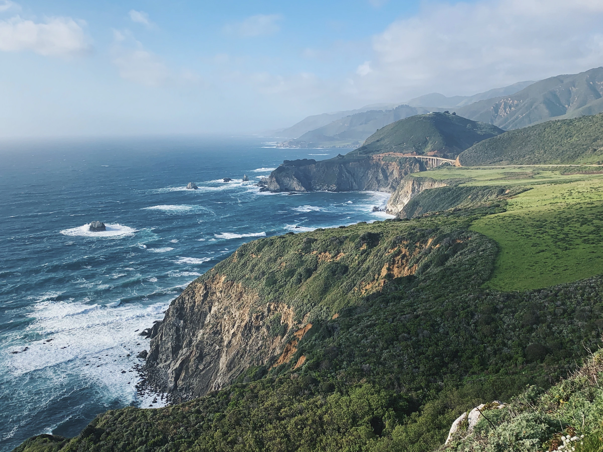 Green coastal cliffs above white surf and the Pacific Ocean