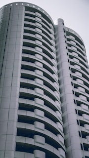 A modern high-rise building with a distinctive curved design featuring multiple balconies. The architecture is sleek and predominantly composed of white and gray tones, conveying a sense of minimalism and contemporary style.