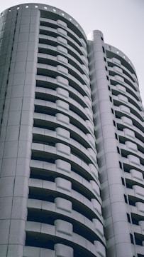 A modern high-rise building with a distinctive curved design featuring multiple balconies. The architecture is sleek and predominantly composed of white and gray tones, conveying a sense of minimalism and contemporary style.