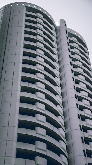 A modern high-rise building with a distinctive curved design featuring multiple balconies. The architecture is sleek and predominantly composed of white and gray tones, conveying a sense of minimalism and contemporary style.