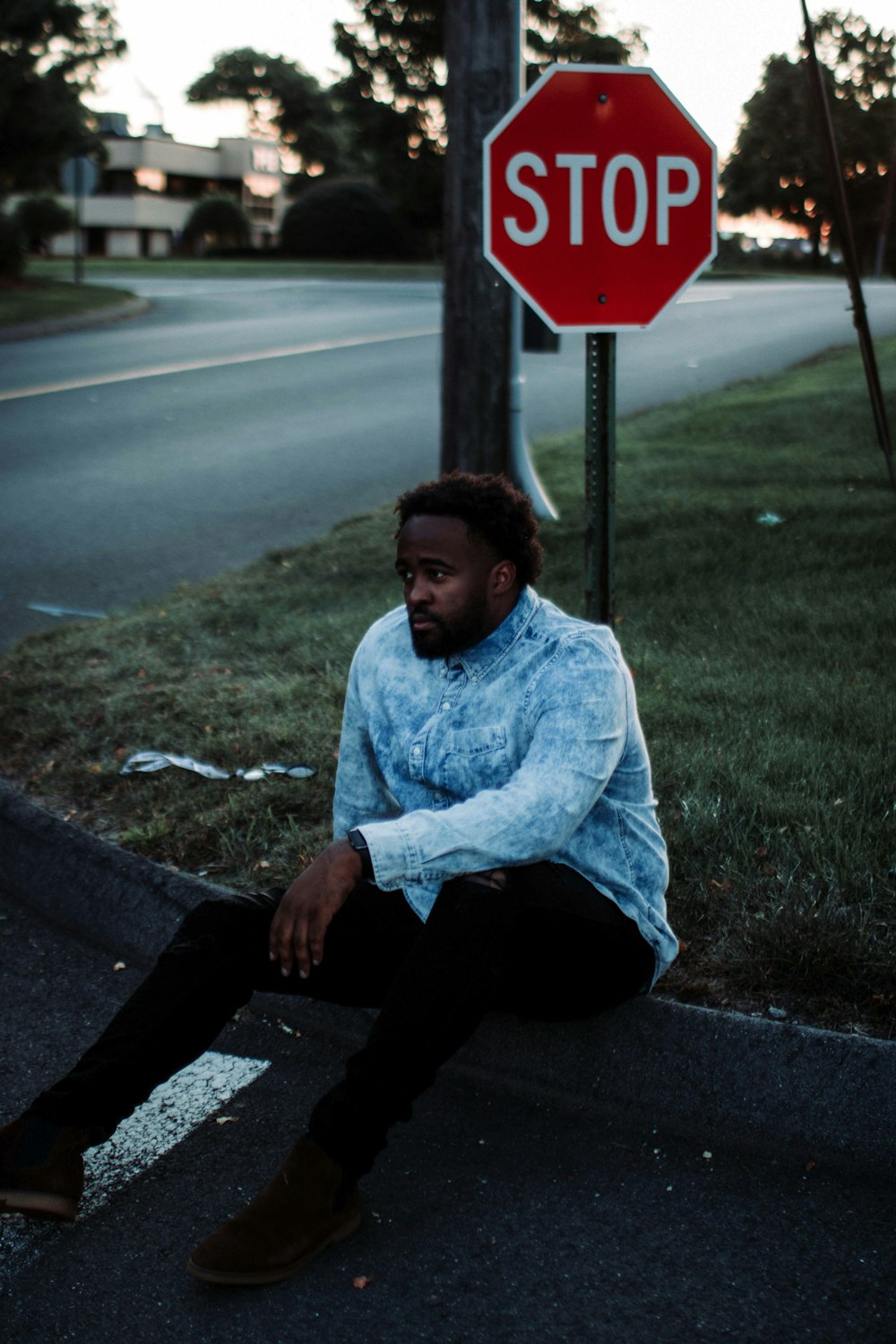 man wearing blue denim jacket sitting besides stop signboard