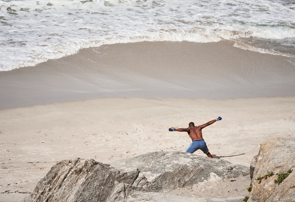 man wearing blue board short walking on seashore