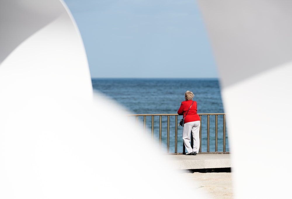 donna in camicia rossa a maniche lunghe che guarda lo specchio d'acqua