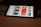 A smartphone displaying a streaming app interface, showing various movie and TV show thumbnails. The screen includes categories like 'For you' and 'New release hit films', with images from popular films. The background is a dimly lit setting with a fabric surface.