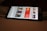 A smartphone displaying a streaming app interface, showing various movie and TV show thumbnails. The screen includes categories like 'For you' and 'New release hit films', with images from popular films. The background is a dimly lit setting with a fabric surface.