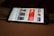 A smartphone displaying a streaming app interface, showing various movie and TV show thumbnails. The screen includes categories like 'For you' and 'New release hit films', with images from popular films. The background is a dimly lit setting with a fabric surface.