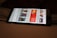 A smartphone displaying a streaming app interface, showing various movie and TV show thumbnails. The screen includes categories like 'For you' and 'New release hit films', with images from popular films. The background is a dimly lit setting with a fabric surface.