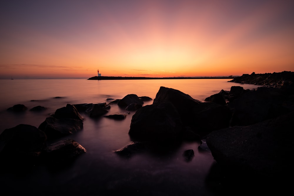 silhouette of rock on body of water during sunset