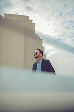 Man wearing classic men's sunglasses standing outdoors with city background.