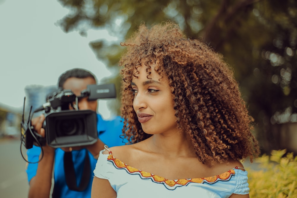 woman smiling and looking at her right in front of man using video camera