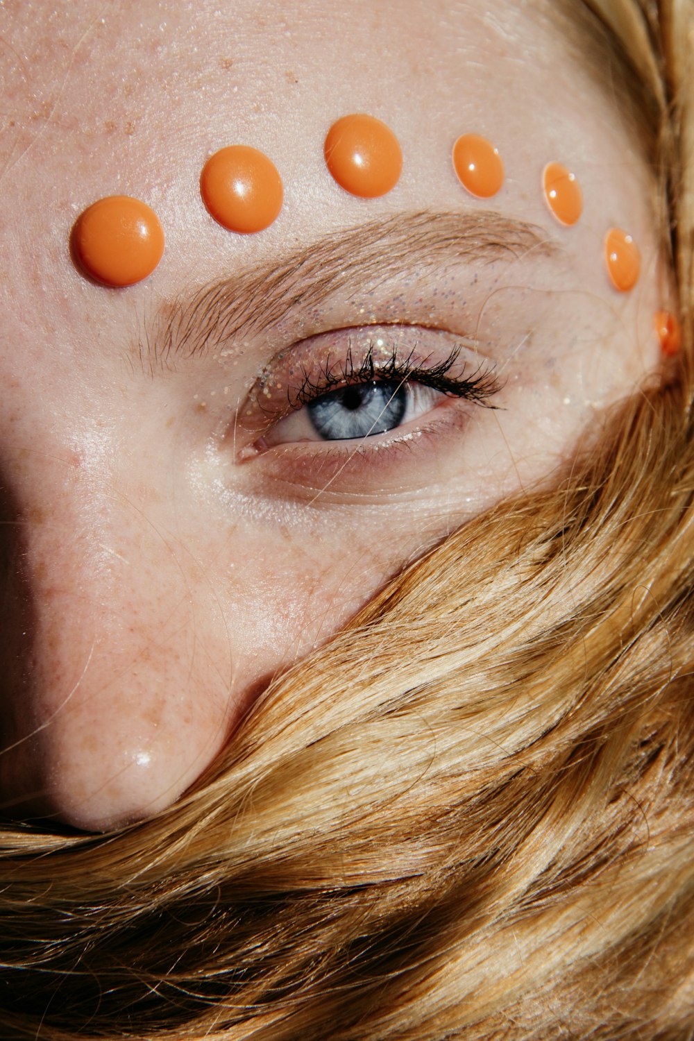 foto de closeup de mulher de cabelos castanhos com contas laranjas em sua sobrancelha esquerda