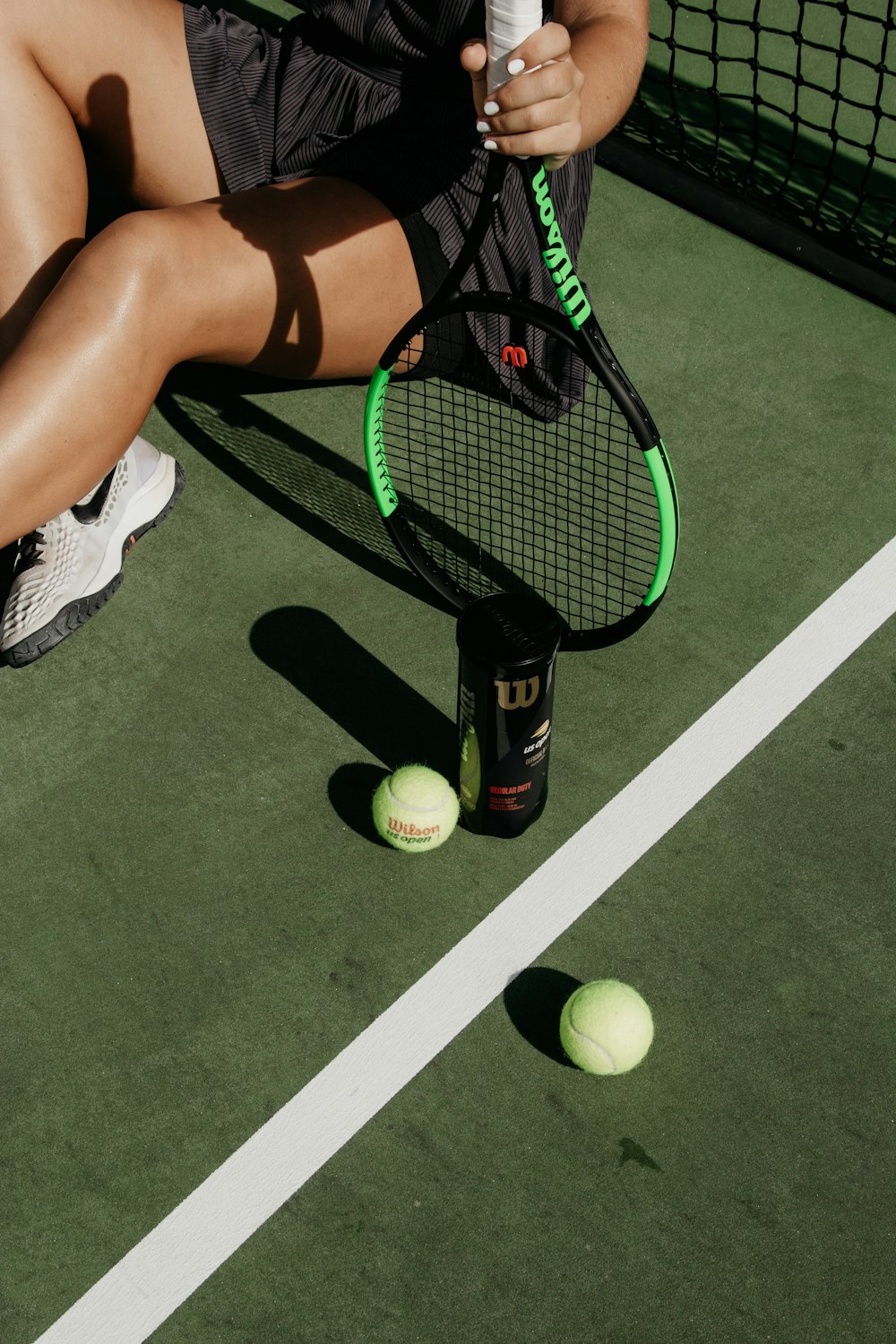 Frau sitzt, während sie Tennisschläger neben Bällen hält