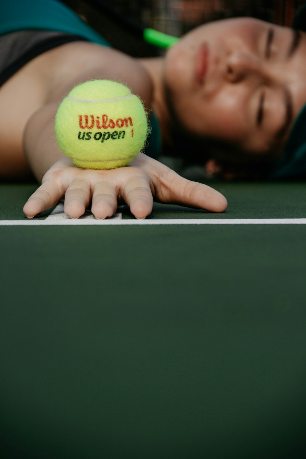 woman lying on tennis court holding green Wilson ball